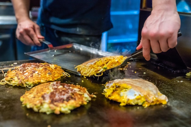 el chef está cocinando Okonomiyaki en la placa de hierro, está usando la espátula para poner la comida en el plato que ya está lista