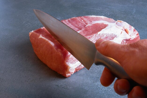 El chef está cortando carne cruda fresca en filetes de primer plano sobre un fondo gris