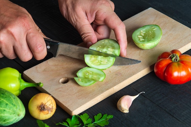 El chef está cortando pepino maduro para ensalada en la cocina del restaurante Primer plano de las manos del cocinero durante el trabajo