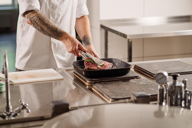 Chef está fritando um bife na panela na cozinha do restaurante