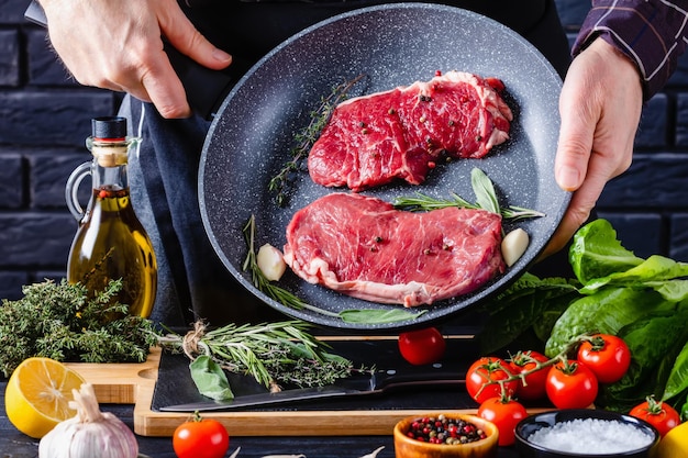 Chef está segurando frigideira com bifes de carne crua