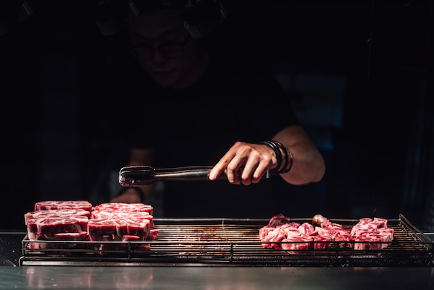 El chef está seleccionando un cubo de carne cruda por pinzas para cocinar con soplete en medio raro.