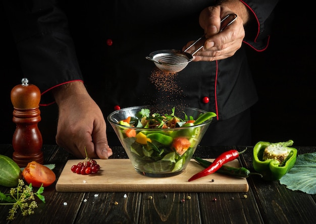 Chef experiente adiciona sabor à salada de legumes Comida vegetariana pelas mãos do cozinheiro na cozinha Ideia de menu para um hotel ou restaurante