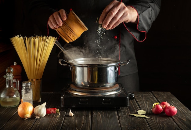 Chef experiente adiciona sal à panela de água fervente Cozinhando espaguete italiano na cozinha