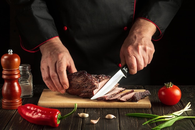 Chef experiente corta a carne assada em uma tábua A ideia de preparar um delicioso almoço