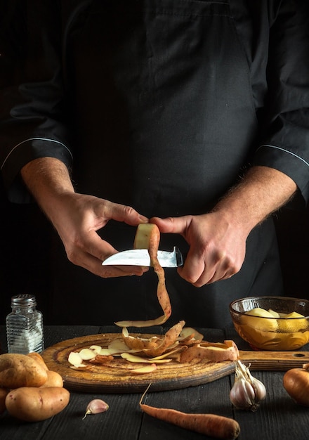 Chef experiente descasca batatas cruas na cozinha de um hotel antes de preparar um prato nacional