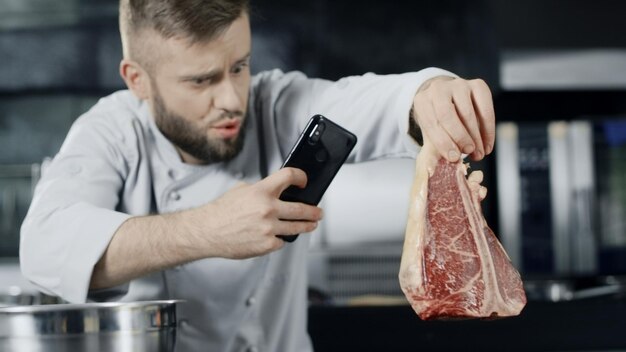 Foto chef fazendo foto de carne com telefone celular chef masculino tirando foto de bife