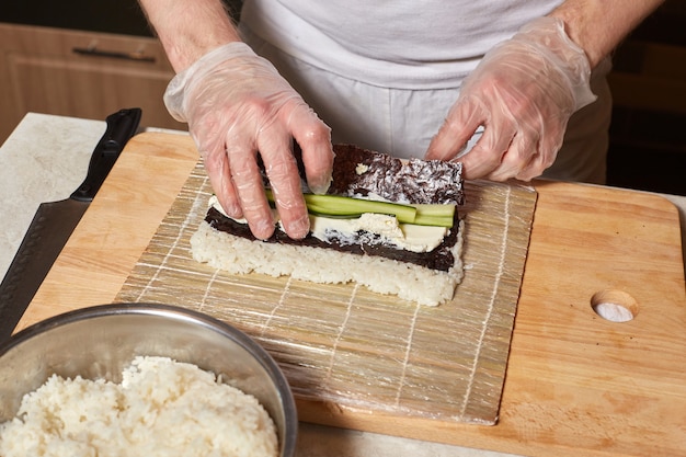 Chef fazendo sushi. Preparando pãezinhos com nori, arroz e pepino