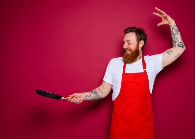 Chef feliz com barba e avental vermelho cozinha com panela