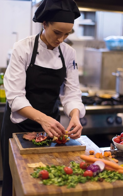 Chef femenina en la cocina del hotel o restaurante preparando filete de ternera con decoración vegetal