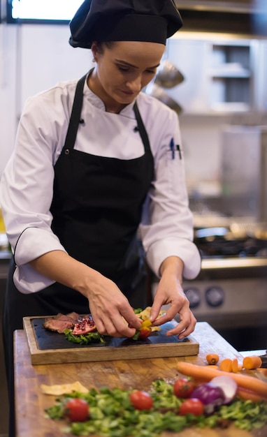 Chef femenina en la cocina del hotel o restaurante preparando filete de ternera con decoración vegetal