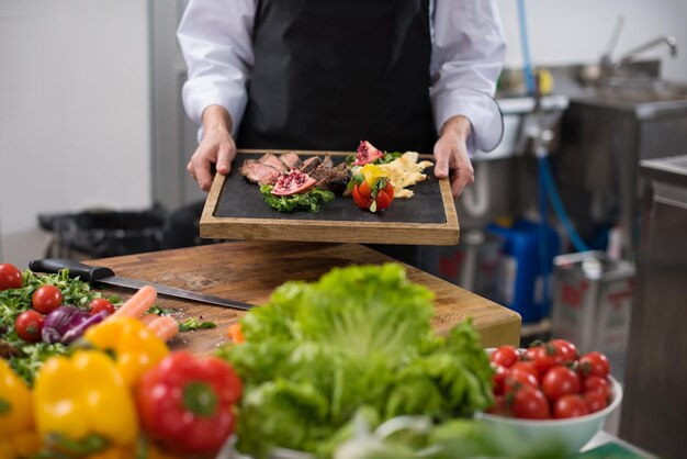 Chef femenina en la cocina del hotel o restaurante sosteniendo un plato de bistec de ternera a la parrilla con decoración vegetal