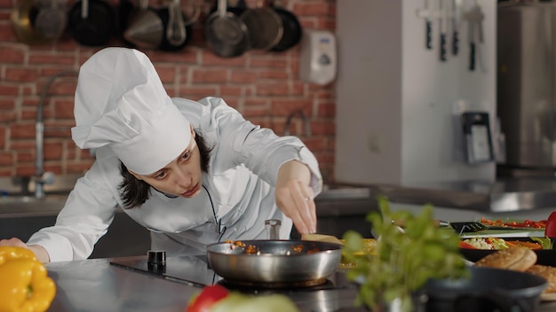 Chef femenina cocinando comida tradicional con queso rallado, agregando queso parmesano orgánico para preparar un plato sabroso. Mujer vertiendo ingrediente triturado para hacer recetas culinarias en la estufa de la cocina.