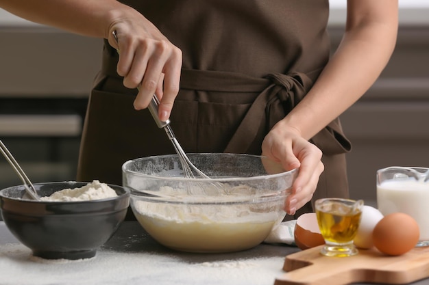 Chef femenina haciendo masa en un tazón de vidrio en la mesa de la cocina