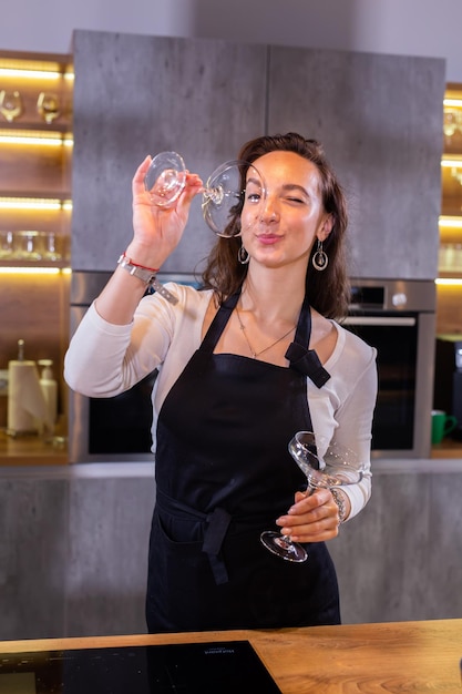 Chef femenina en uniforme sosteniendo copas de vino mientras sonríe y se divierte en la cámara