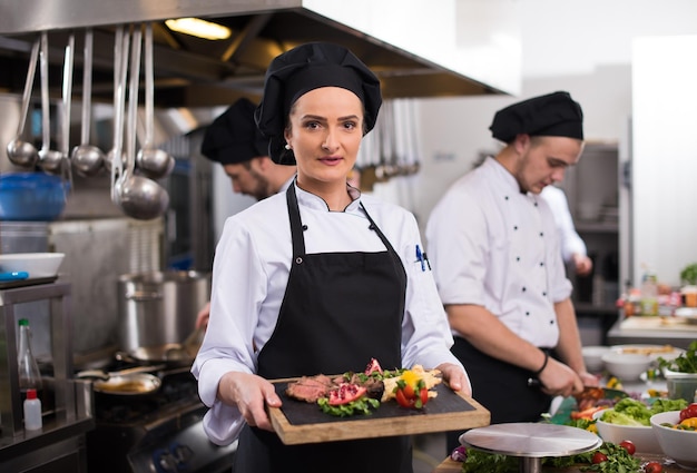 Chef feminina na cozinha de um hotel ou restaurante segurando um prato de bife grelhado com decoração de vegetais