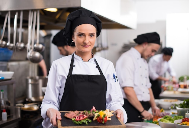 Chef feminina na cozinha de um hotel ou restaurante segurando um prato de bife grelhado com decoração de vegetais