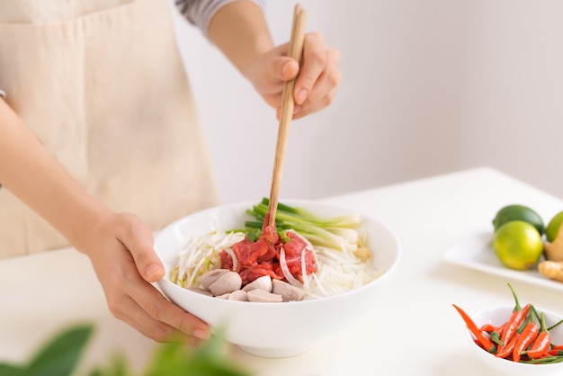 Chef feminina prepara sopa vietnamita tradicional Pho bo com ervas, carne e macarrão de arroz