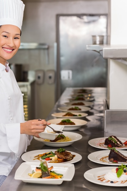 Chef feminino sorridente que enfeita comida na cozinha