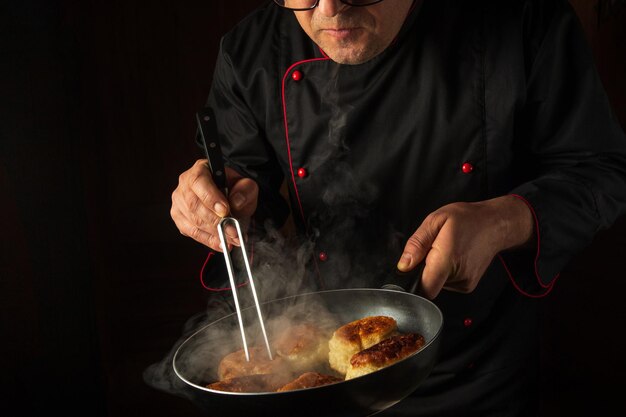 Foto el chef frita rosquillas en la cocina de un restaurante un tenedor en la mano de un cocinero y una sartén