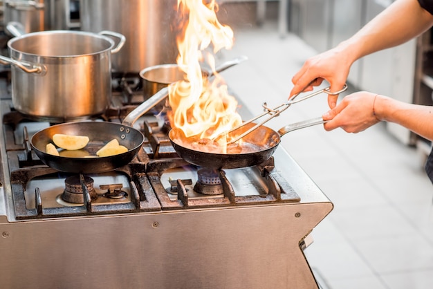 Chef fritando bife de carne no fogão a gás com fogo na cozinha. vista de perto na frigideira