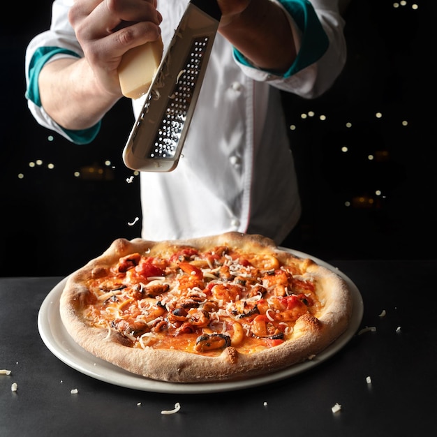 Chef frota queso en pizza con mariscos en un fondo negro Cocina Mediterránea