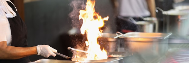 Chef en guantes de goma está cocinando en primer plano de fuego