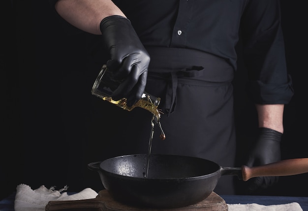 Chef con guantes de látex negro vierte el aceite de oliva de una botella transparente en una sartén de hierro fundido negro