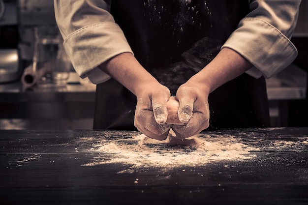 El chef hace masa para pasta en una mesa de madera.