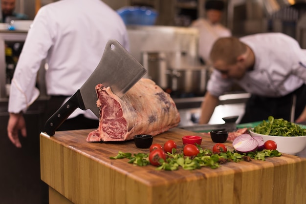 Chef con hacha mientras corta un gran trozo de carne de vacuno sobre una placa de madera en la cocina del restaurante