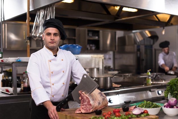 Chef con hacha mientras corta un gran trozo de carne de vacuno sobre una placa de madera en la cocina del restaurante