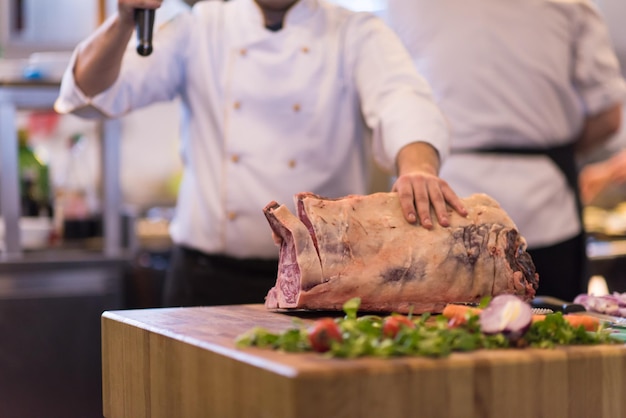 Chef con hacha mientras corta un gran trozo de carne de vacuno sobre una placa de madera en la cocina del restaurante
