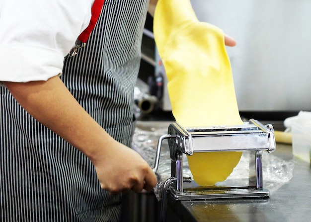 Foto chef haciendo masa para pastelería, pasta fresca y máquina de pasta en la cocina