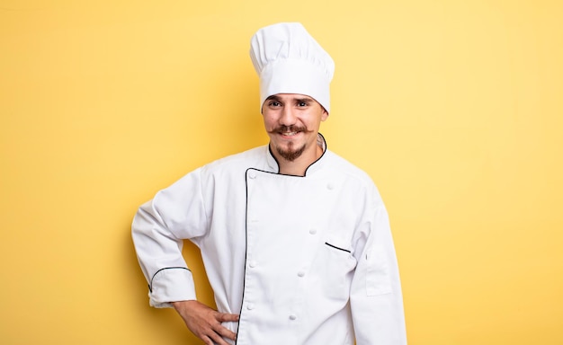 Chef hombre sonriendo felizmente con una mano en la cadera y confiado