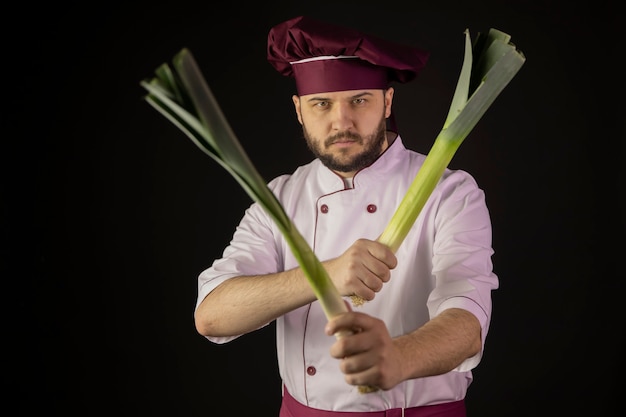 Chef hombre en uniforme tiene dos tallos de puerro cruzándolos como arma