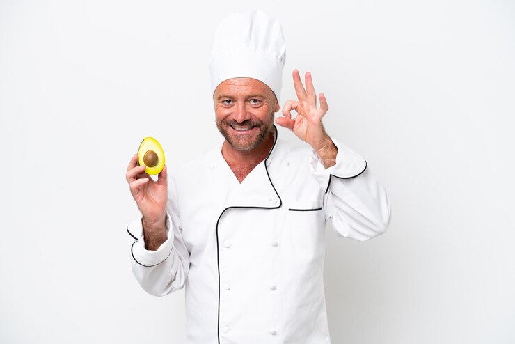 Foto chef homem segurando um abacate isolado no fundo branco mostrando sinal de ok com os dedos