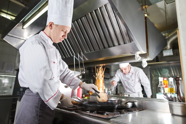 Chef in der Restaurantküche am Ofen mit der Wanne, kochend