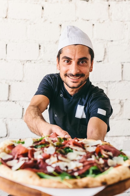 Chef italiano sonriente o pizzaiolo que ofrece pizza en el restaurante