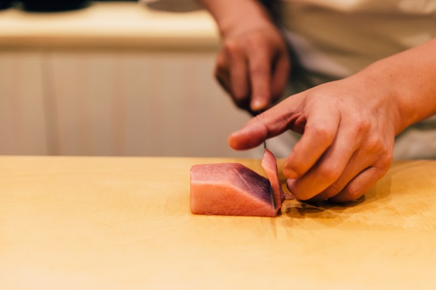 El chef japonés Omakase cortó el atún rojo graso mediano (Chutoro en japonés) cuidadosamente con un cuchillo en la encimera de madera para hacer sushi. Comida japonesa de lujo.