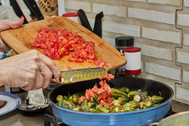 Chef joga tomates na panela com quiabo e cebola roxa frita