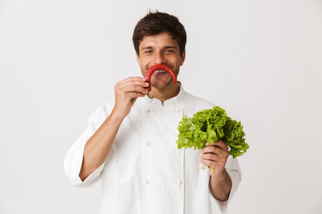 Chef joven emocional aislado en blanco con ensalada y ají.