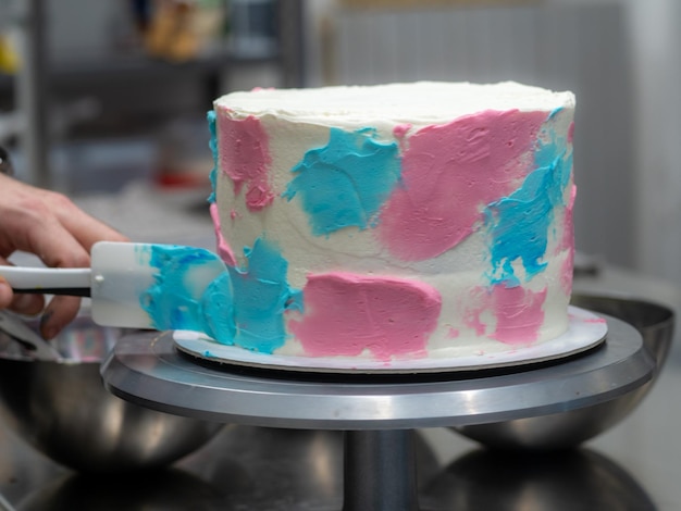 Chef-Konditor-Designer konfektioniert einen 3-stöckigen Kuchen mit Milchglasur, dekoriert mit cremigen Pastellfarben