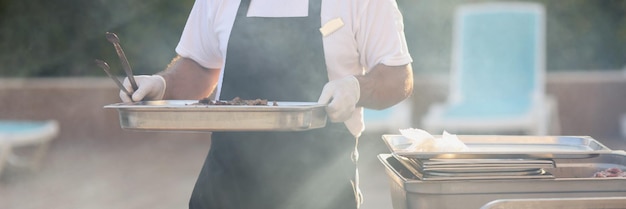 El chef lleva una construcción de metal de comida cocinada para freír alimentos, hacer un picnic a la parrilla al aire libre