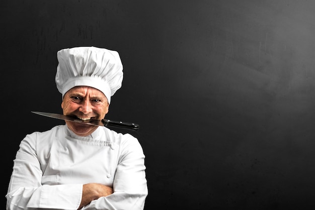 Chef louco com uma faca entre os dentes isolada em um fundo escuro