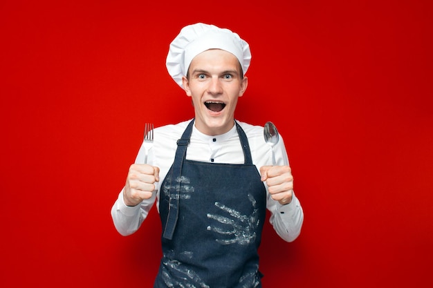 Chef maluco de uniforme segura colher e garfo em trabalhador de cozinha de fundo isolado vermelho