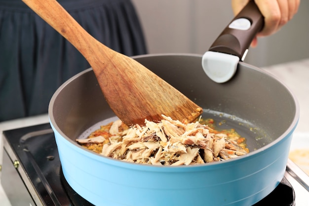 Chef mano femenina asiática cocinando Pampis Tongkol, atún desmenuzado con sabor picante. Proceso de cocción en la cocina