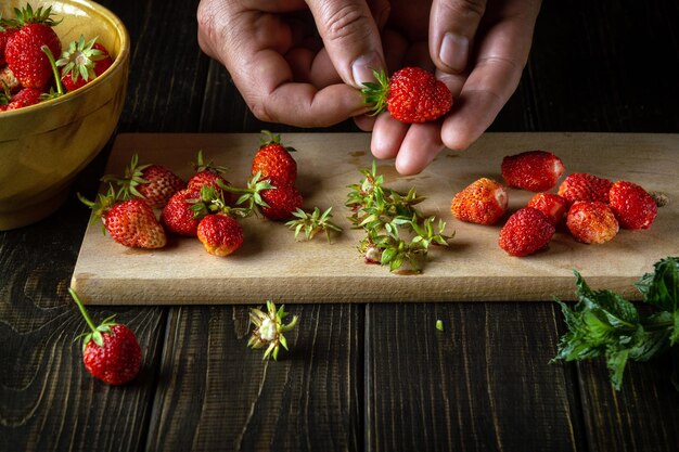 Chef de manos clasificando fresas frescas en la tabla de cortar de la cocina para preparar un refresco con menta Postres de dieta de cocina