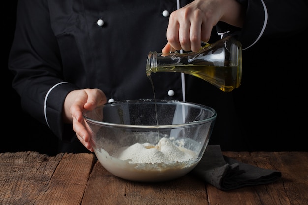 Chef manos vierte el aceite de oliva en un tazón de masa cruda.