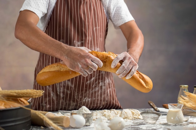 Chef mantém o pão fresco na mão. Homem preparando pães na mesa na cozinha.