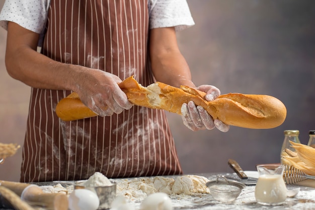 Chef mantém o pão fresco na mão. Homem preparando pães na mesa na cozinha.